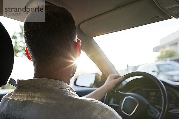 Rückansicht eines jungen Mannes  der bei Sonnenuntergang Auto fährt