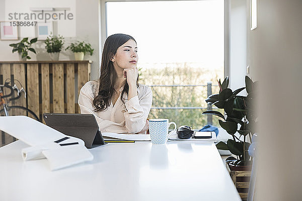 Junge Frau sitzt zu Hause am Tisch und schaut zur Seite