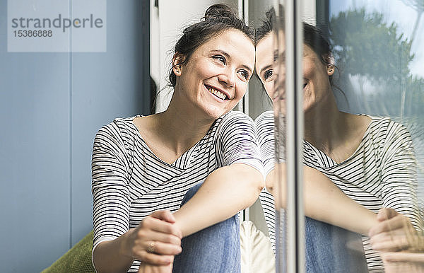 Lächelnde Frau  die zu Hause aus dem Fenster schaut