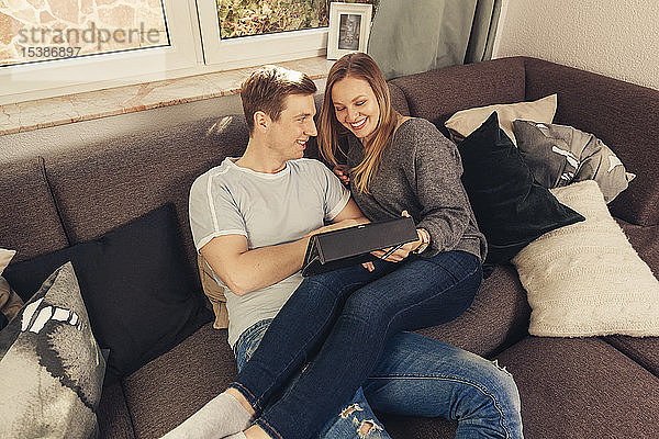 Junges Paar entspannt sich auf dem Sofa und benutzt ein Tablett