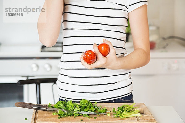 Mädchen steht in der Küche und hält Tomaten  Teilansicht