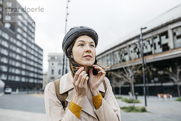 Porträt einer Frau  die in der Stadt einen Fahrradhelm aufsetzt
