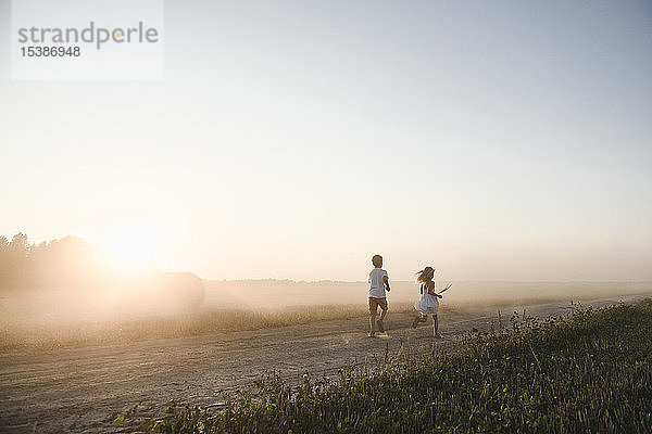 Mädchen und Junge rennen auf einem ländlichen Feldweg