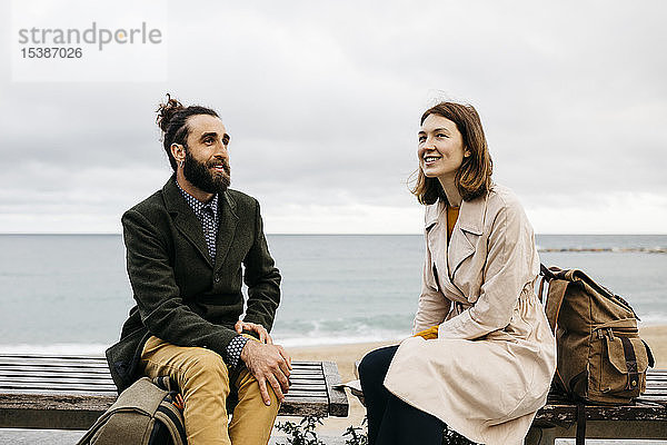 Lächelndes Paar sitzt auf einer Bank an der Strandpromenade und unterhält