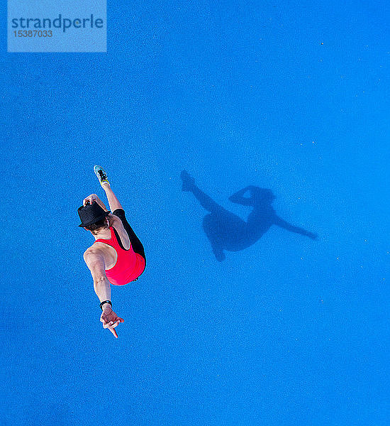 Springende junge Frau und ihr Schatten auf blauem Hintergrund  Draufsicht