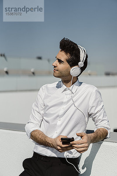 Geschäftsmann  der auf der Dachterrasse mit Kopfhörern und Smartphone Musik hört