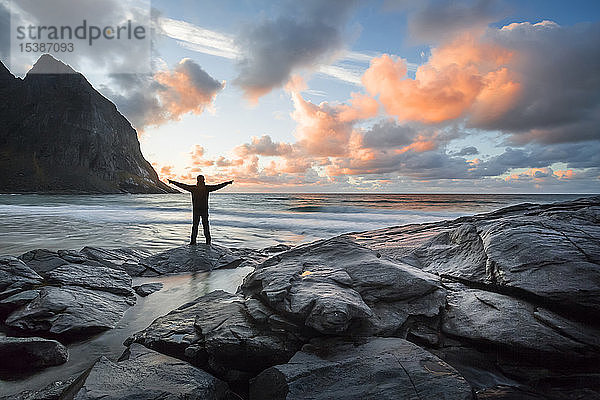 Norwegen  Lofoten  Mann mit erhobenen Armen am Abend am Strand von Kvalvika