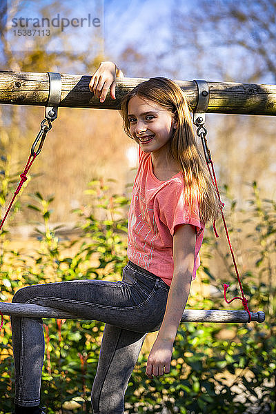Porträt eines lächelnden Mädchens  das auf einer Gymnastikstange im Garten sitzt