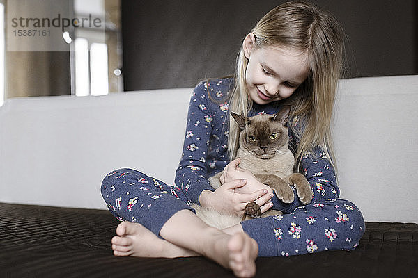 Lächelndes kleines Mädchen in Pyjama mit Blumenmuster zu Hause mit Katze