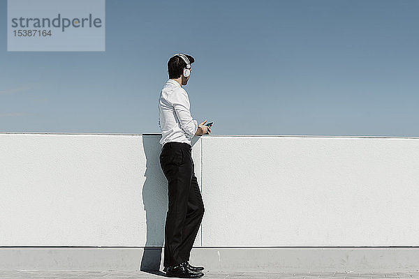 Geschäftsmann  der auf der Dachterrasse mit Kopfhörern und Smartphone Musik hört