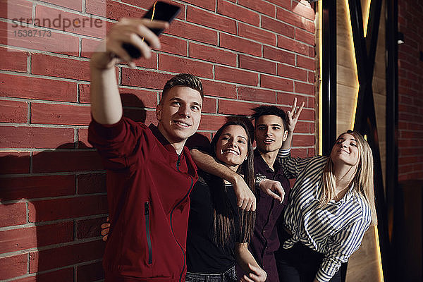 Glückliche Freunde beim Selfie mit Smartphone an der Ziegelmauer