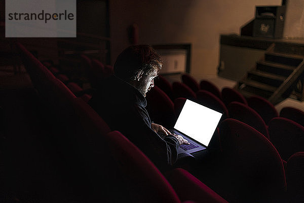 Regisseur sitzt im Theatersaal und arbeitet am Laptop