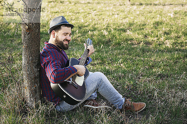 Mann spielt Gitarre an einem Baum auf einer Wiese
