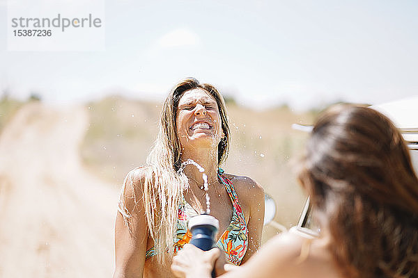 Zwei glückliche junge Frauen im Bikini  die Wasser spritzen