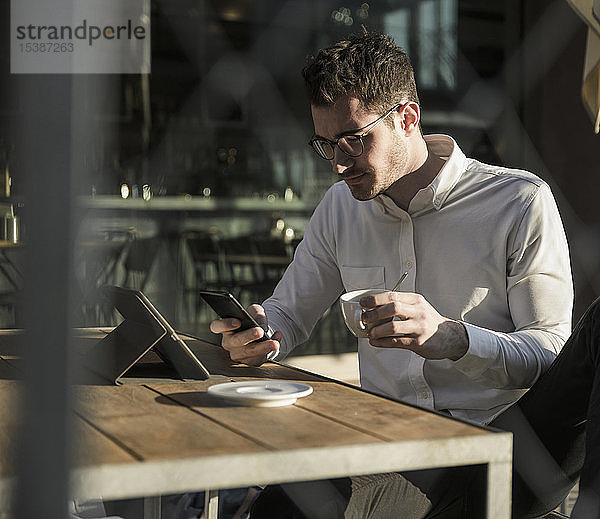 Junger Mann benutzt Handy und Tablet im Strassencafé