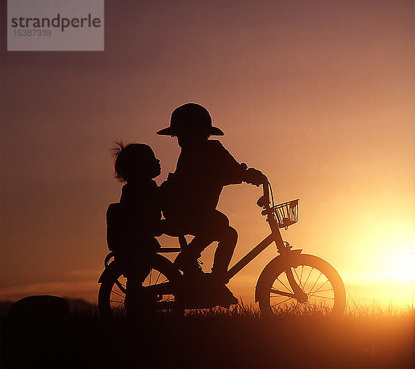 Silhouette von zwei Kindern beim Fahrradfahren im Sonnenuntergang