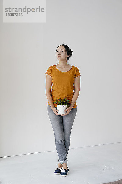 Junge Frau steht an einer Wand und hält eine Topfpflanze