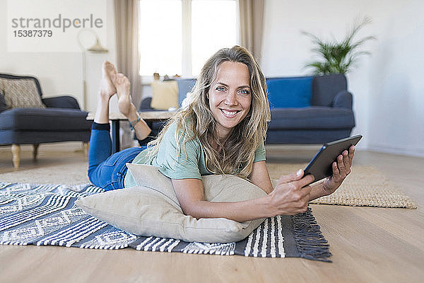 Porträt einer lächelnden Frau  die zu Hause mit einem Tablett auf dem Boden liegt