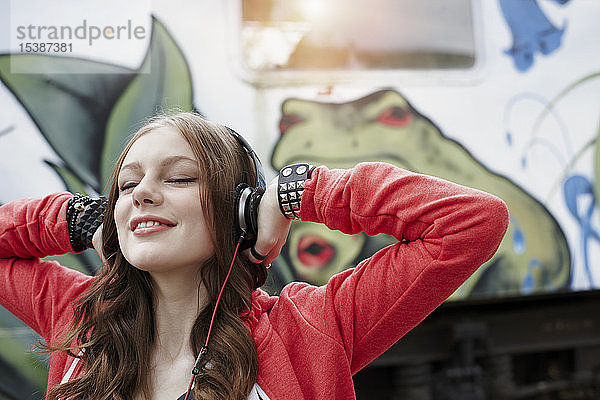 Porträt einer Teenagerin mit Kopfhörern an einem bemalten Zugwaggon
