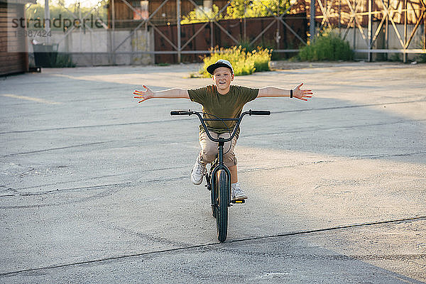 Porträt eines lächelnden Jungen  der freihändig auf einem bmx-Fahrrad fährt