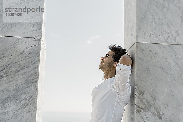 Mann mit weißem Hemd lehnt an Marmorsäule und schaut nach oben