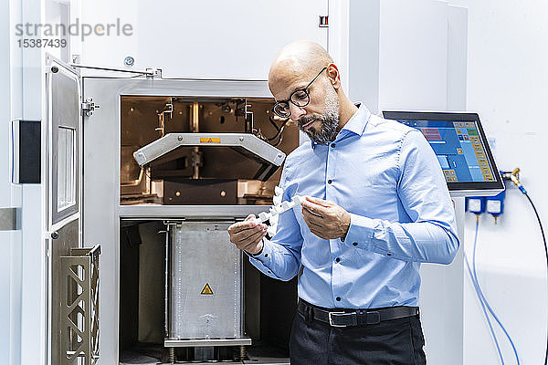 Mann hält Werkstück am 3D-Drucker