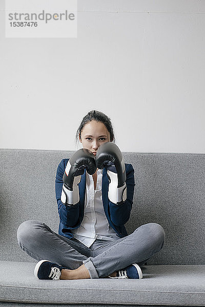 Porträt einer jungen Frau  die auf einer Couch sitzt und Boxhandschuhe trägt