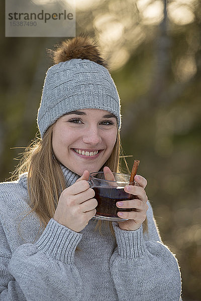 Porträt einer glücklichen jungen Frau mit einer Tasse Tee im Wald