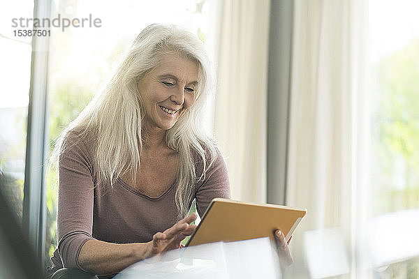 Porträt einer glücklichen  reifen Frau  die zu Hause ein digitales Tablet benutzt