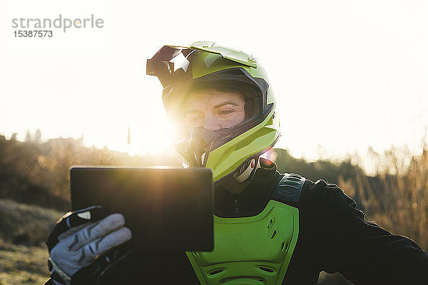 Porträt eines Motocross-Fahrers  der bei Sonnenuntergang auf das Tablet schaut