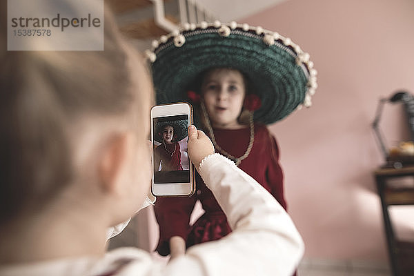 Kleines Mädchen fotografiert verkleidete Schwester mit Smartphone