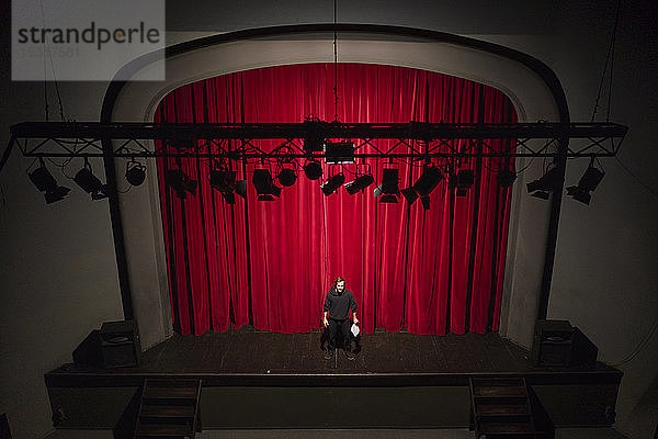 Schauspieler mit Drehbuch steht auf der Theaterbühne vor rotem Vorhang