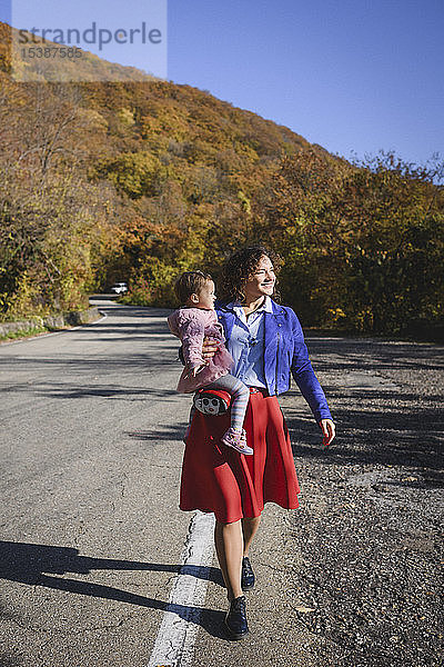 Glückliche Mutter trägt ihre Tochter auf einer Landstraße