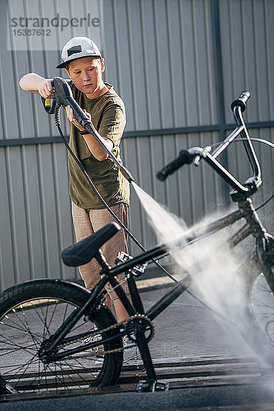Junge wäscht bmx Fahrrad mit Hochdruckreiniger auf dem Hof