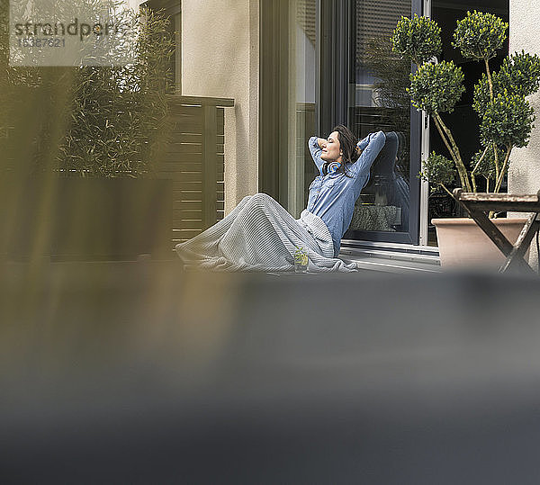 Entspannte  in eine Decke gehüllte Frau sitzt zu Hause auf der Terrasse