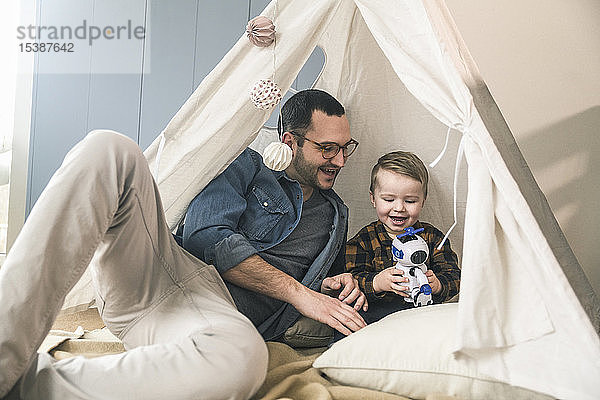 Glückliche Vater und Sohn spielen zu Hause mit einem Roboter im Zelt