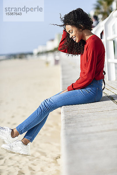 Glückliche junge Frau sitzt an der Strandpromenade