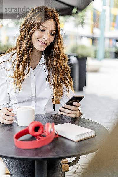 Junge Geschäftsfrau sitzt im Cafe und benutzt ein Smartphone