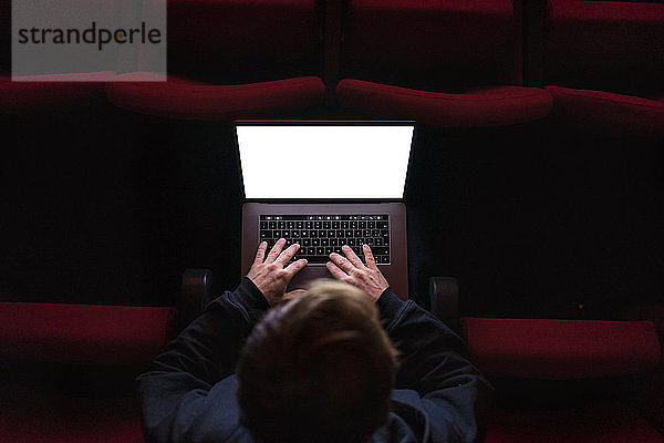 Regisseur sitzt im Theatersaal und arbeitet am Laptop  Draufsicht
