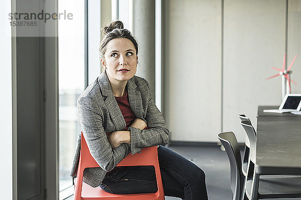 Porträt einer Geschäftsfrau  die auf einem Stuhl im Büro sitzt und zur Seite schaut