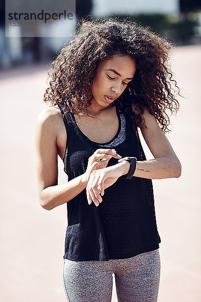 Sportliche junge Frau schaut draußen auf ihre Smartwatch