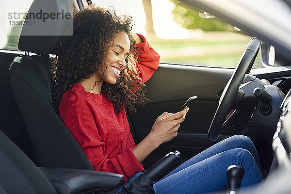 Lächelnde junge Frau benutzt Handy im Auto