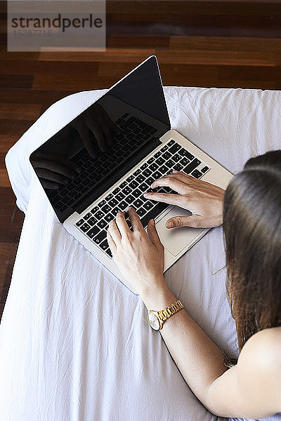 Junge Frau im Bett liegend mit Laptop  Teilansicht