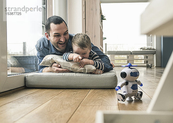 Aufgeregter Vater und Sohn liegen zu Hause auf einer Matratze und schauen einem Spielzeugroboter zu