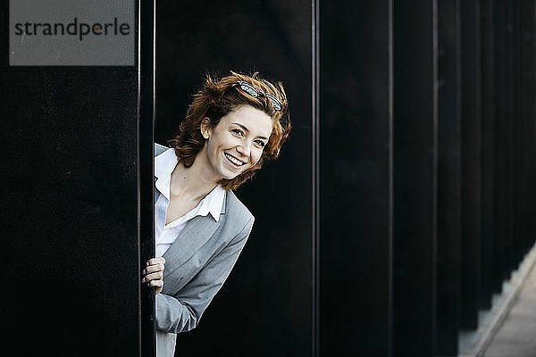 Glückliche junge Geschäftsfrau schaut aus der Fassade eines Bürogebäudes