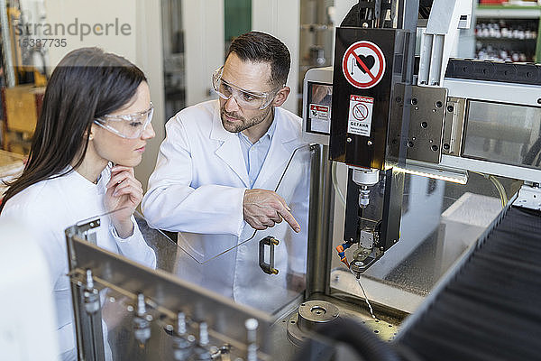 Kollegen tragen Laborkittel und Schutzbrille an der Maschine in einer modernen Fabrik