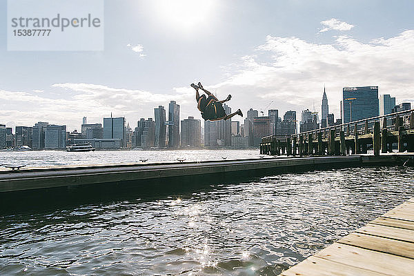 USA  New York  Brooklyn  zwei junge Männer beim Rückwärtssalto auf dem Pier vor der Skyline von Manhattan