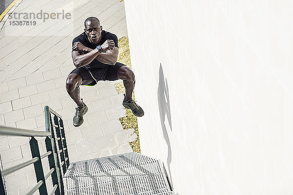Mann in schwarzer Sportkleidung springt auf einer Treppe in die Luft