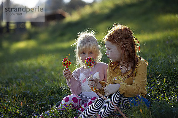 Zwei Schwestern sitzen auf einem Feld und halten Lollipops