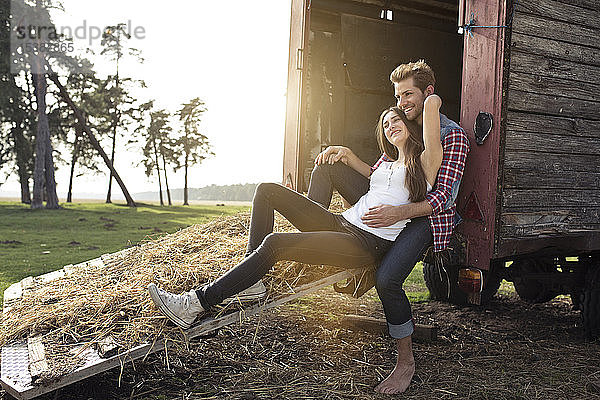 Glückliches junges Paar sitzt auf einem Wohnwagen auf dem Land
